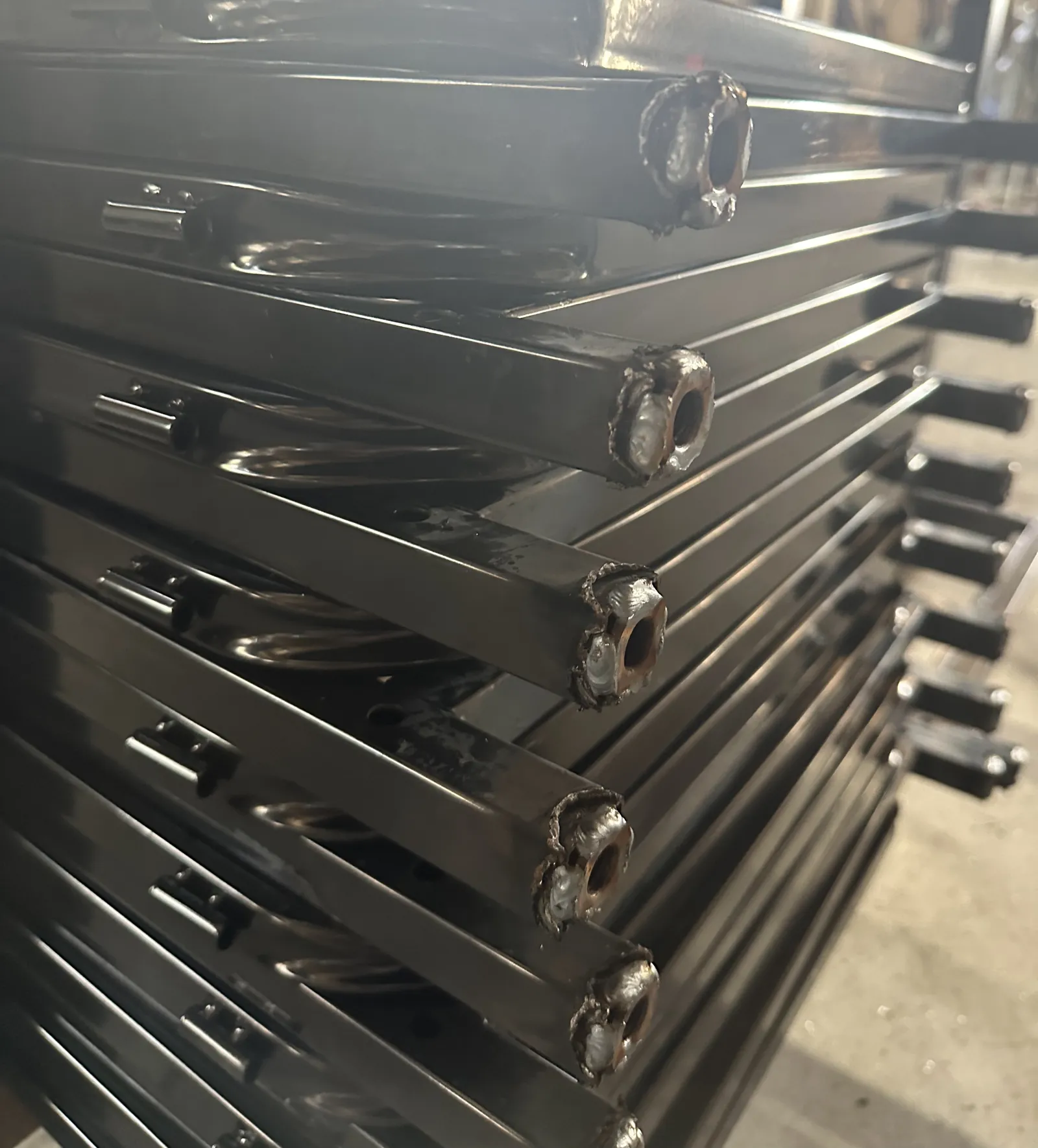 Coated black cart frames stacked after finishing, with castor sockets at the corners